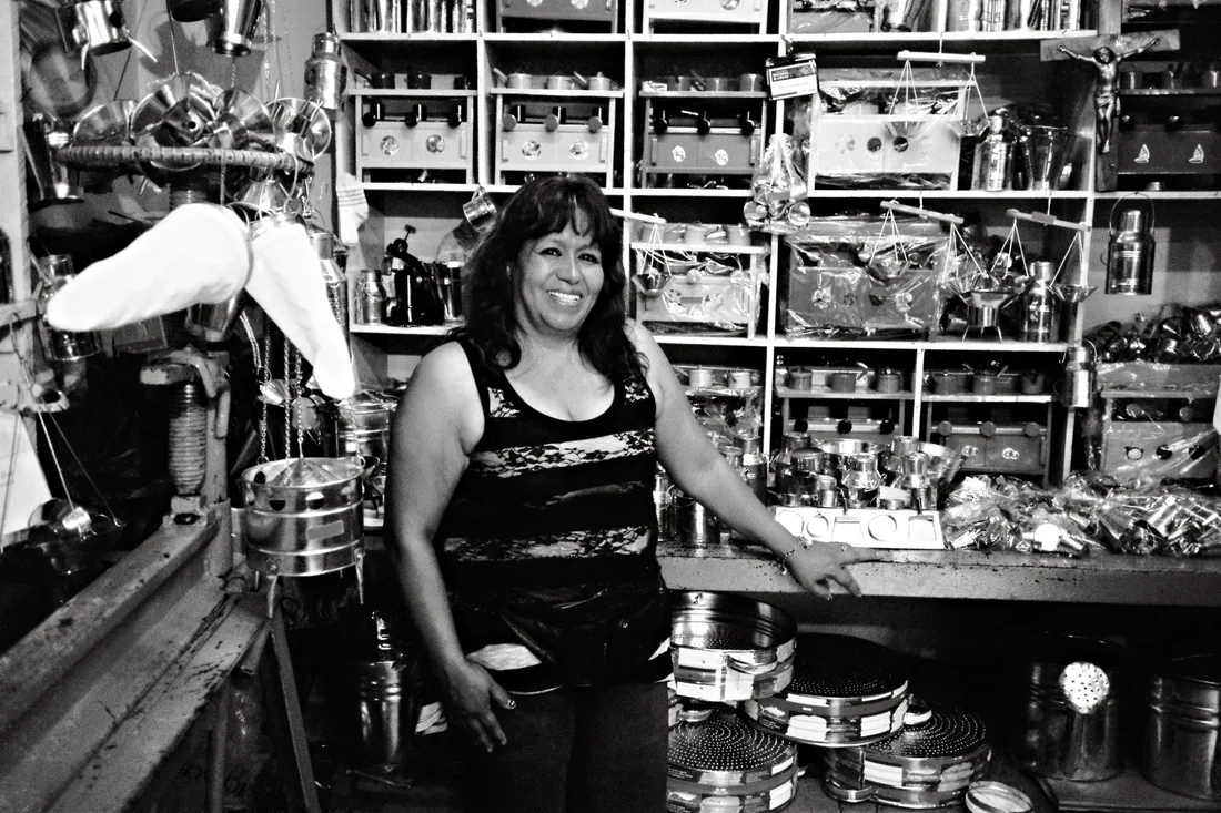 A female shop owner smiling amidst metal goods in a Quito market. Photo by DΛVΞ GΛRCIΛ on Pexels