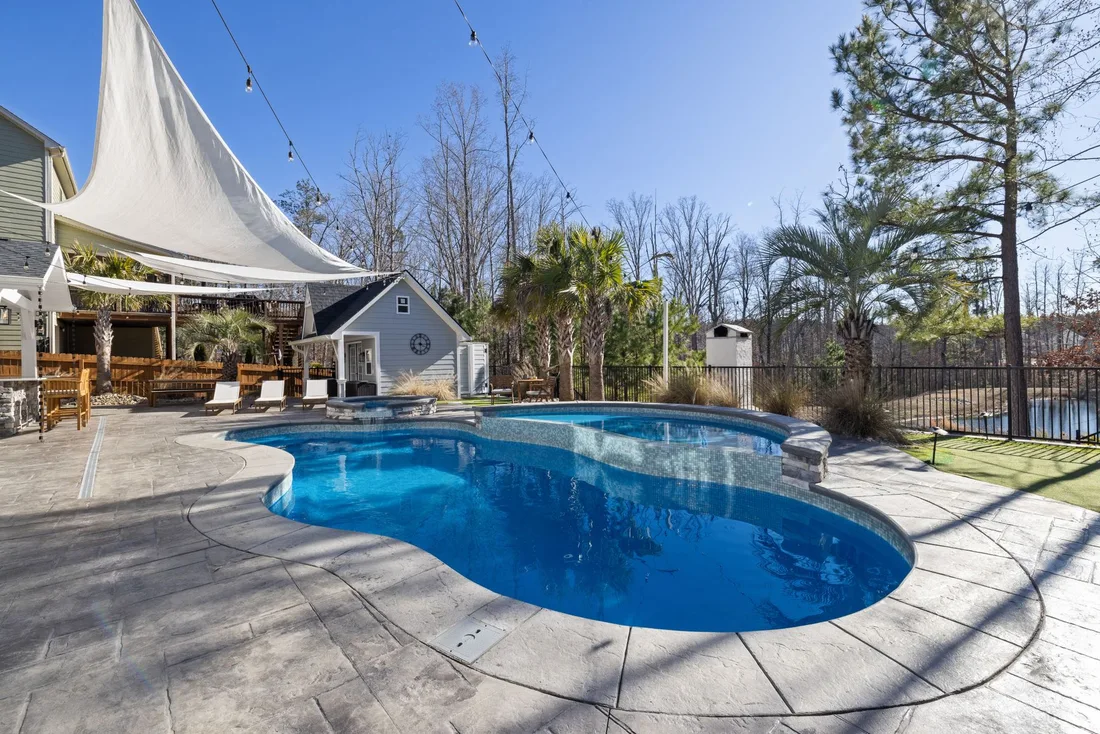 A sunny backyard oasis featuring a luxurious pool, deck, and palm trees, perfect for relaxation. Photo by Curtis Adams on Pexels