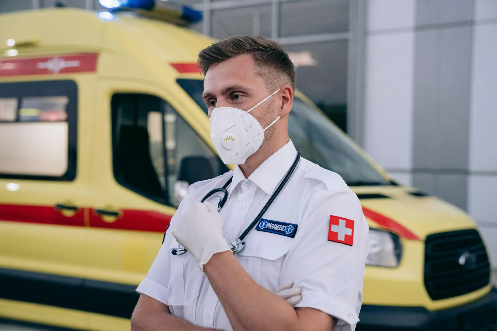 Paramedic wearing a mask and stethoscope standing confidently in front of an ambulance. Photo by Mikhail Nilov on Pexels
