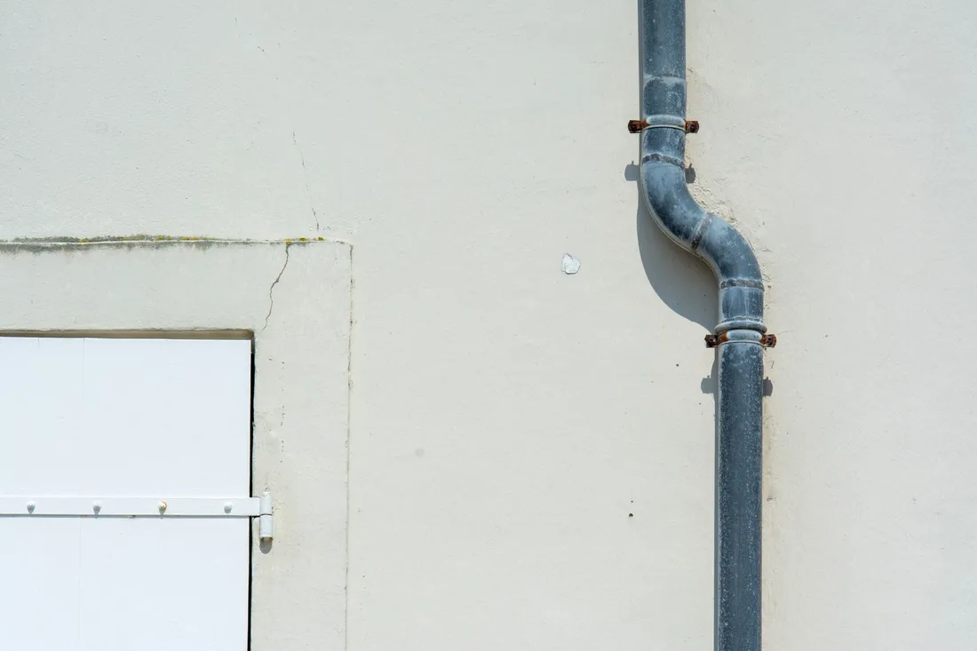 Gray vertical vent pipe running down a white exterior wall. Photo by Jan van der Wolf on Pexels