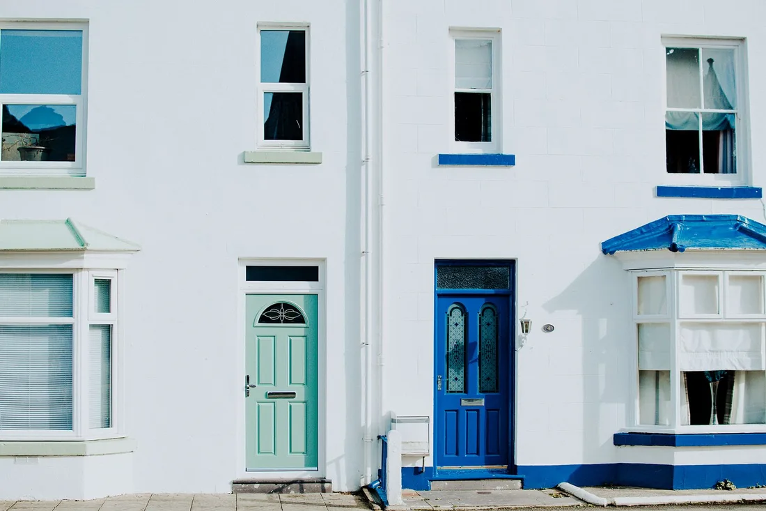White rendered house facade with blue trim, windows and colorful front doors. Photo by Lisa Fotios on Pexels