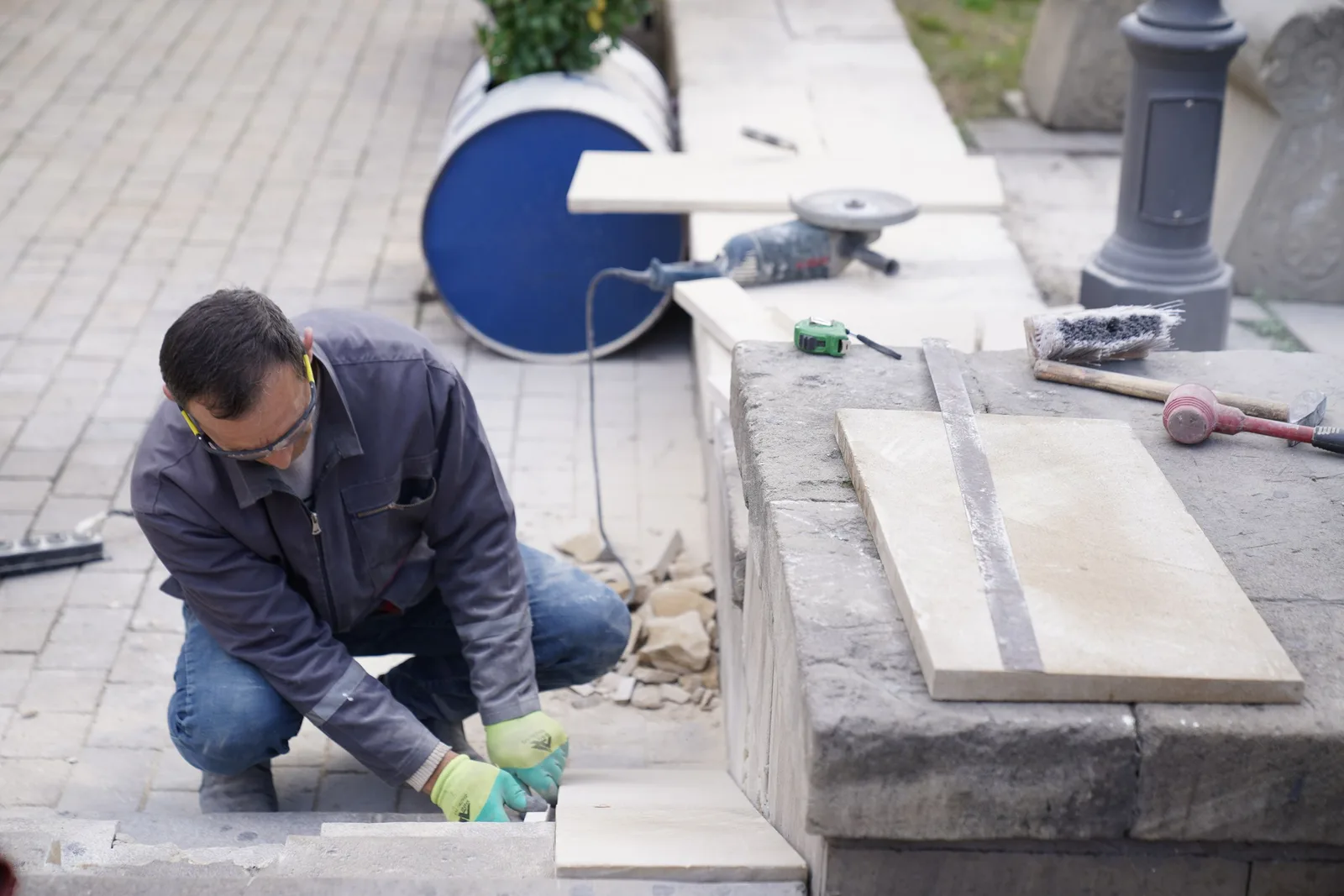 Mason kneeling at a stone masonry job laying and cutting paving stone with tools. Photo by Tahir Xəlfəquliyev on Pexels