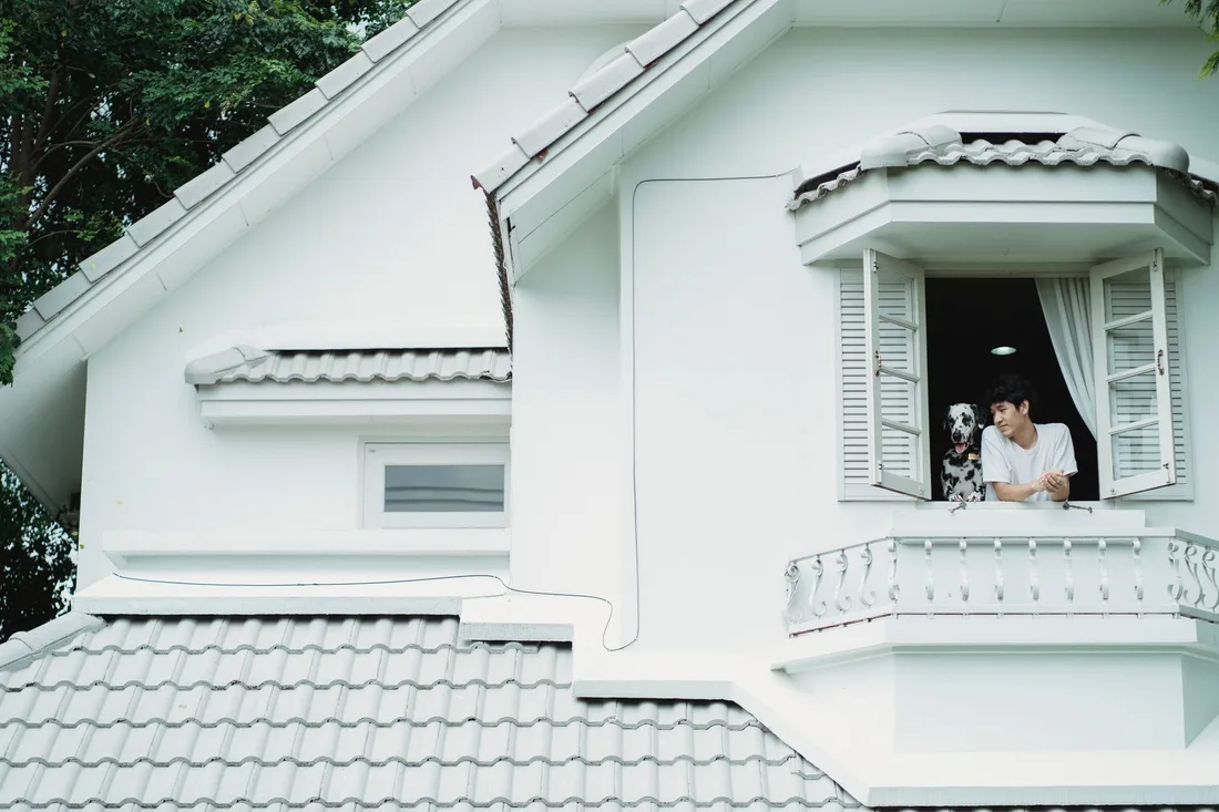 White house with a tiled roof and a resident looking out of an upstairs window. Photo by Bethany Ferr on Pexels