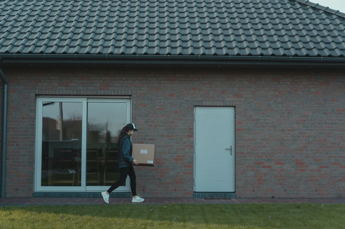 A courier delivers a package to a modern brick house, showcasing logistics in action. Photo by Tima Miroshnichenko on Pexels
