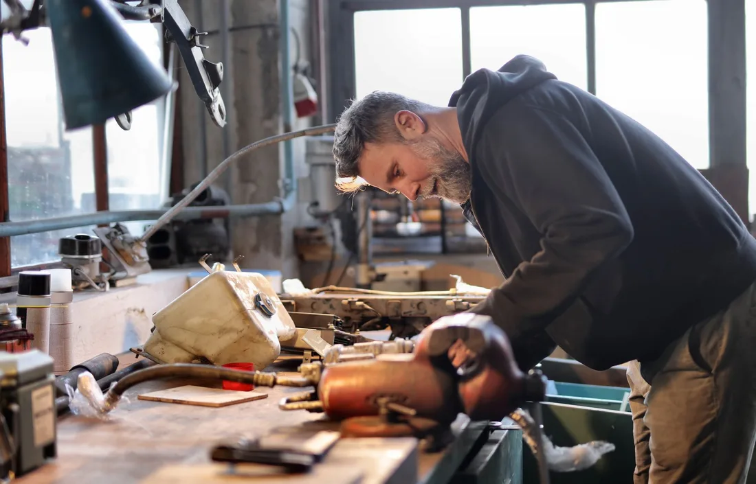 Side view of brutal male worker in casual wear standing at workbench and fixing metal details while using tools and working in workshop. Photo by Andrea Piacquadio on Pexels