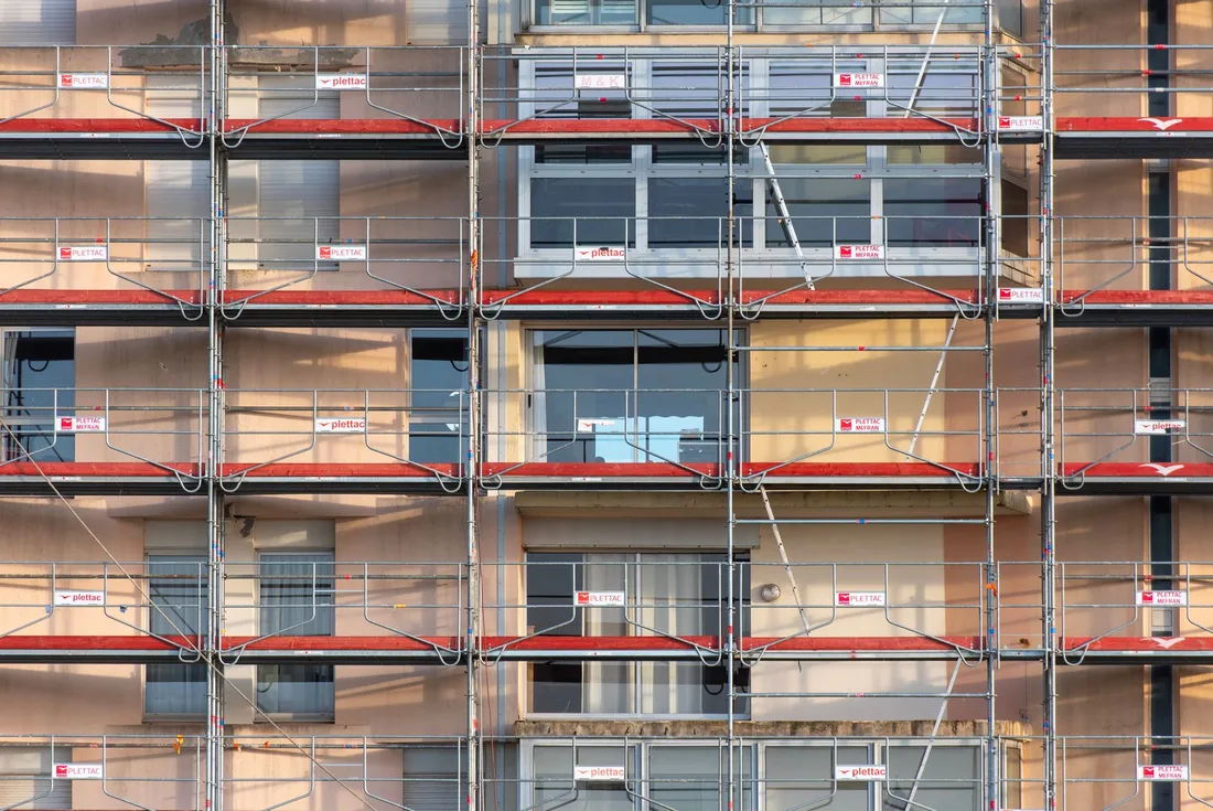 Multi-story apartment building facade covered in scaffolding with red railings. Photo by Jan van der Wolf on Pexels