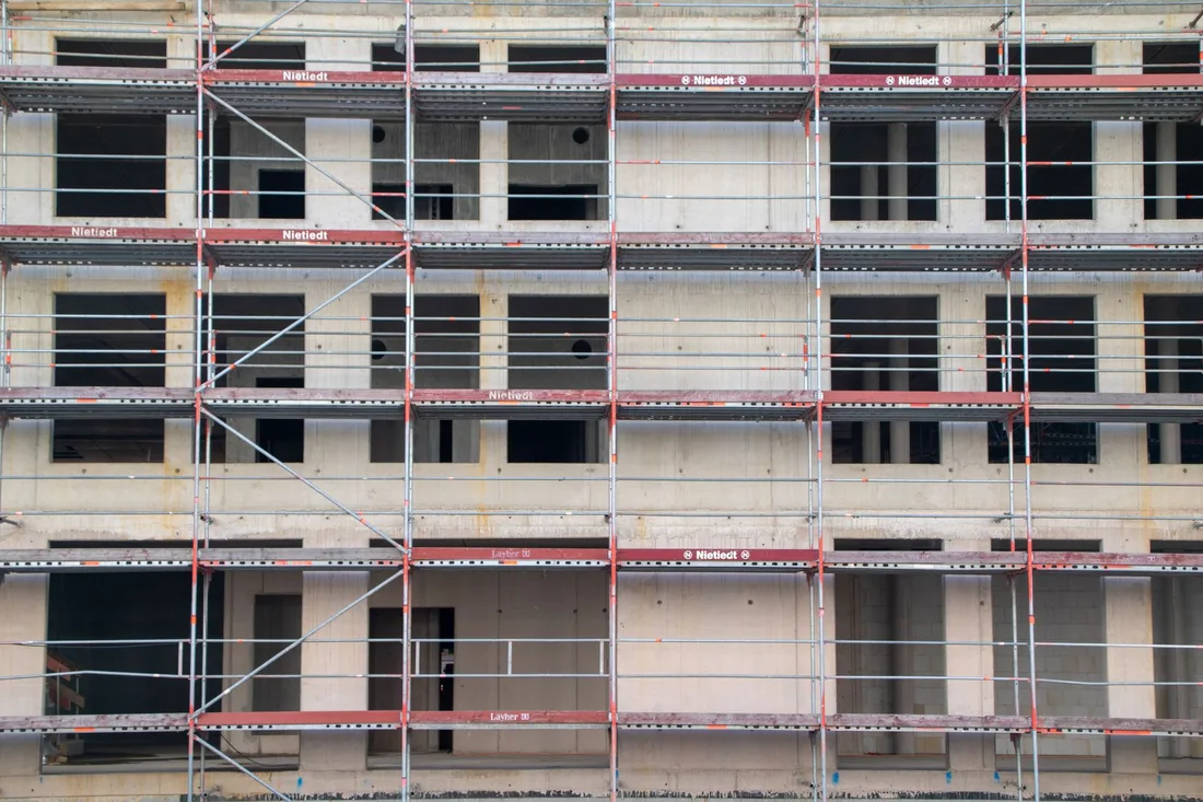 Building exterior wrapped in scaffolding with red guard rails on every floor. Photo by Frank Rietsch on Pexels
