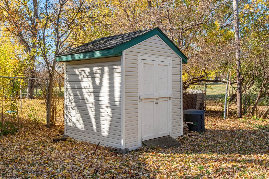 White wooden garden shed with green roof in a leafy backyard with autumn leaves. Photo by Đỗ Huy Hoàng on Pexels