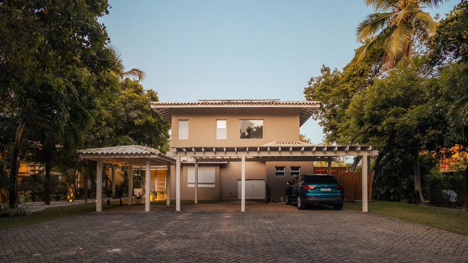 Exterior view of a modern house with a driveway and palm trees at sunset, offering a serene tropical ambiance. Photo by Alef Morais on Pexels
