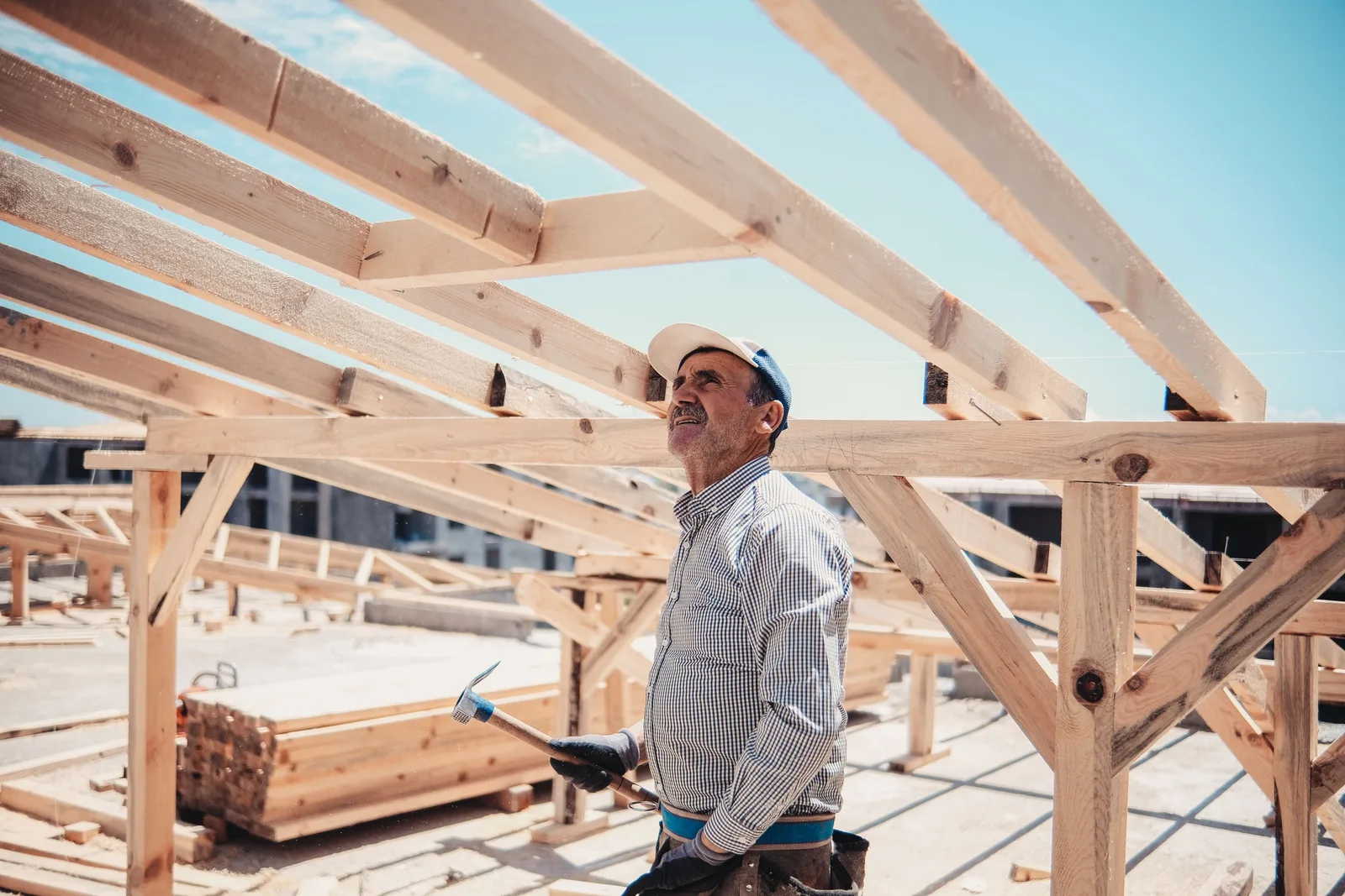 Carpenter in a cap standing on a timber frame structure under construction against a blue sky. Photo by SERHAT  TUĞ on Pexels