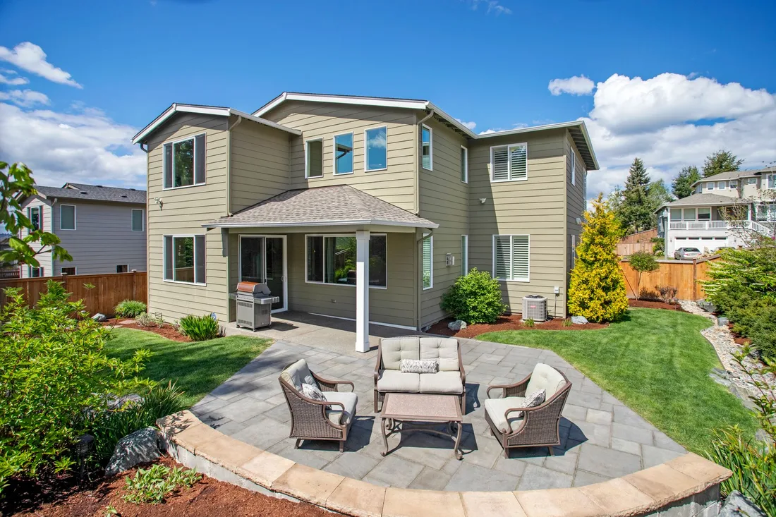 Finished stone patio with outdoor seating area beside a two-story house with a green lawn. Photo by Spencer Lee Eiseman on Pexels
