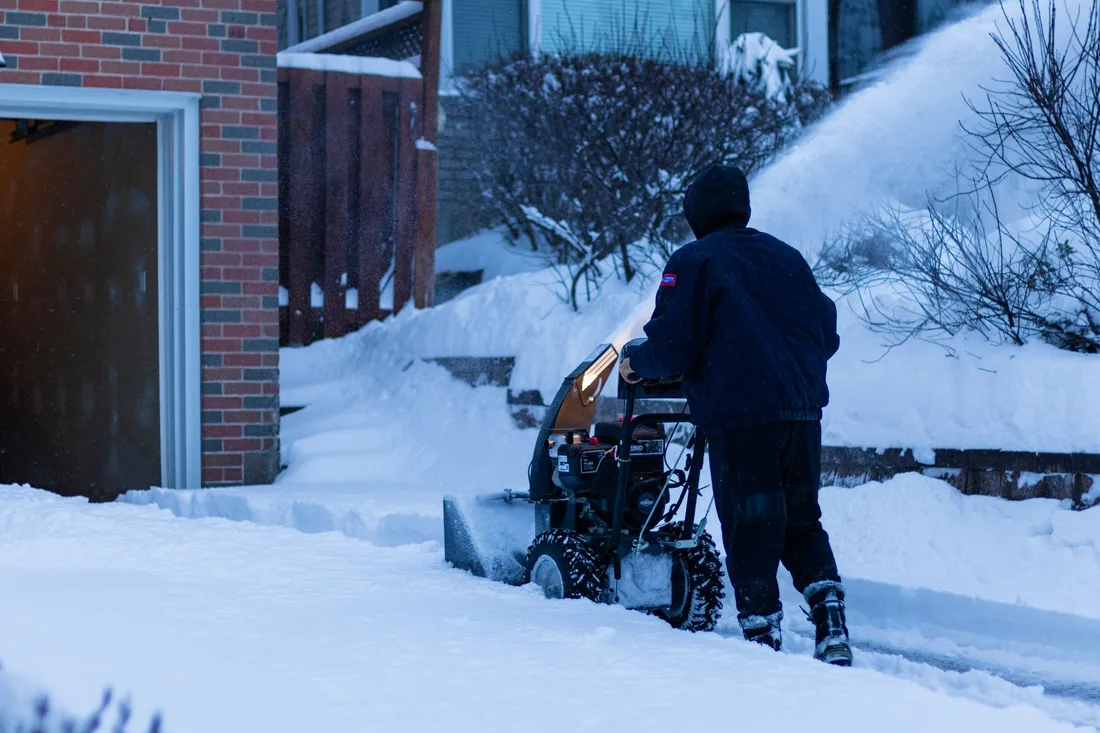 Man clearing a driveway with a snow blower beside a brick house. Photo by Anurag Jamwal on Pexels