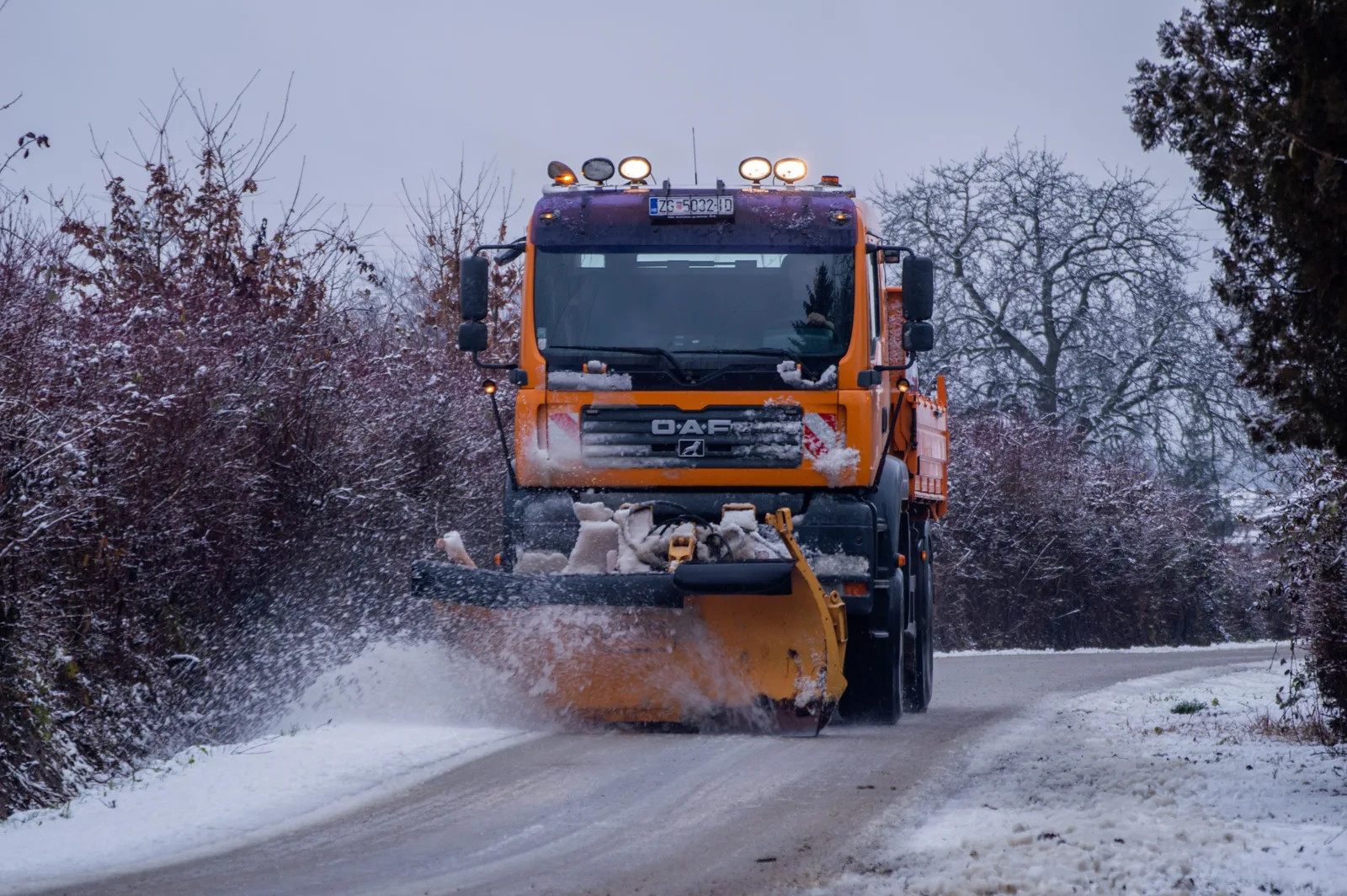 Orange snow plow truck clearing a snowy road with snow spraying. Photo by Anton Kudryashov on Pexels