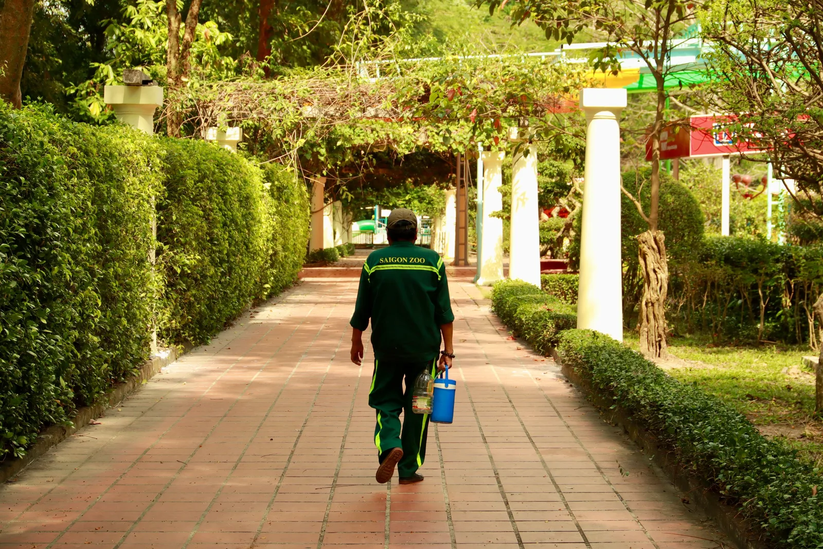 Pest control technician in green uniform carrying a sprayer along a garden path in Australia. Photo by Tuan Vy on Pexels
