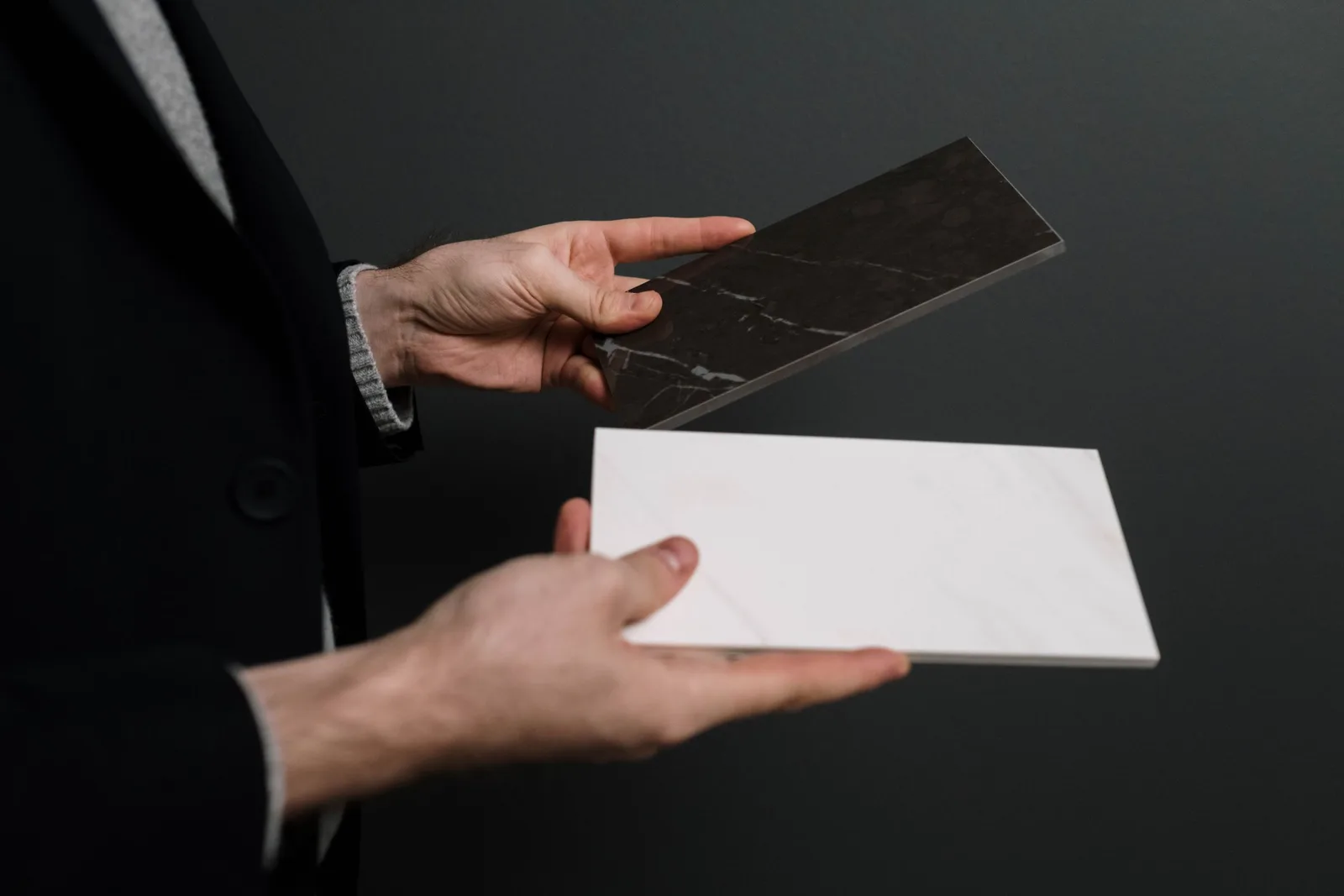 Close-up of hands holding two contrasting marble and stone tiles. Photo by cottonbro studio on Pexels