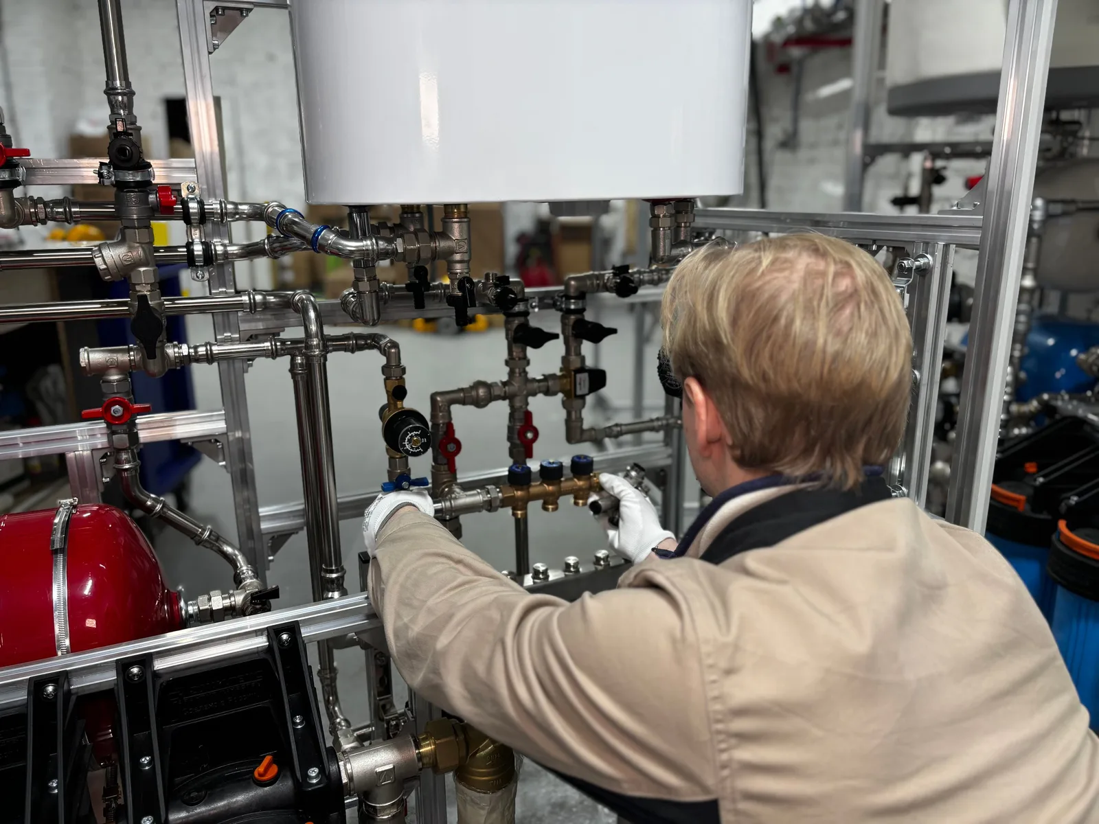 Technician in a beige jacket adjusting pipework on a water heating system. Photo by МОБО Модульные Котельные on Pexels