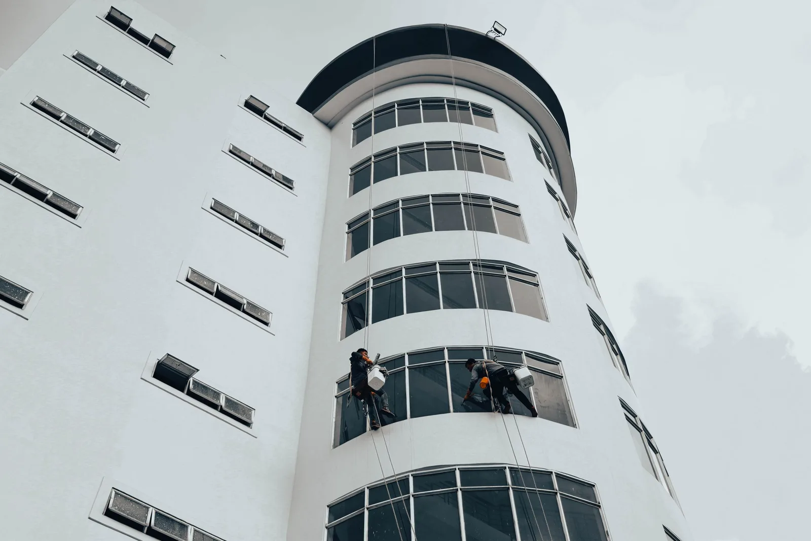 Workers cleaning windows on a modern high-rise building using ropes. Urban architectural maintenance. Photo by Manh Cuong Le on Pexels