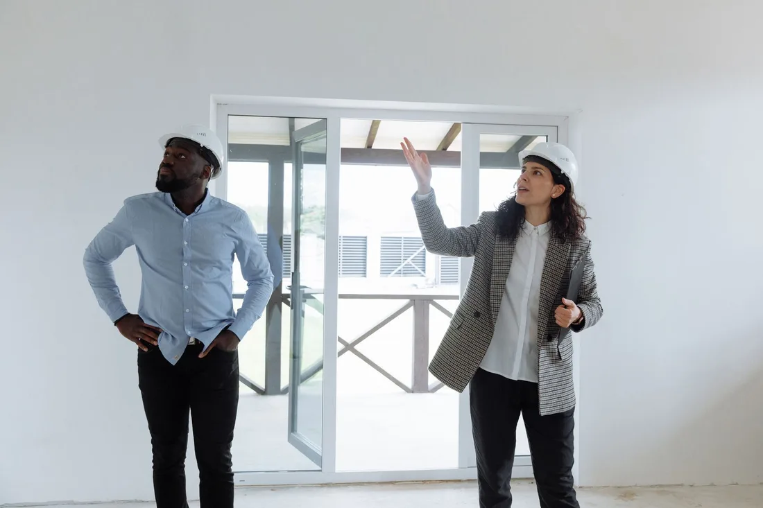 Two contractors inspecting a modern house interior wearing hard hats. Photo by Thirdman on Pexels