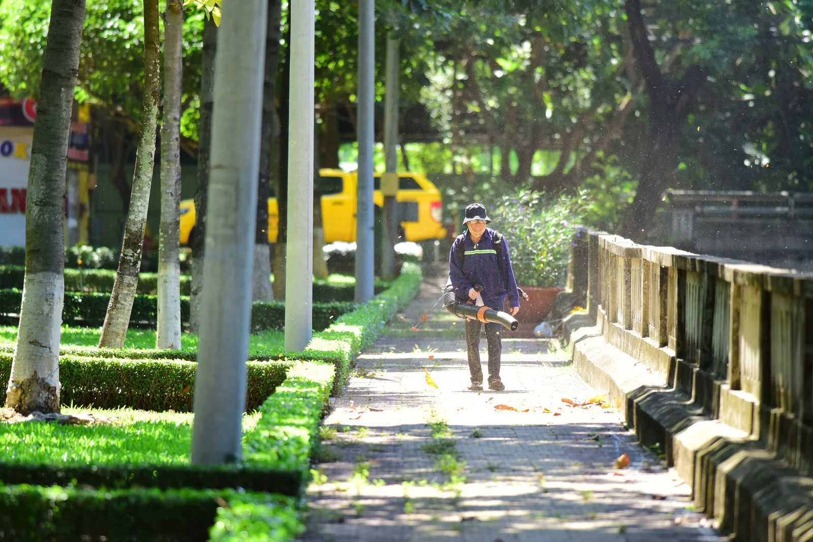 Person with leaf blower maintaining cleanliness in a sunlit park walkway. Photo by Sóc Năng Động on Pexels