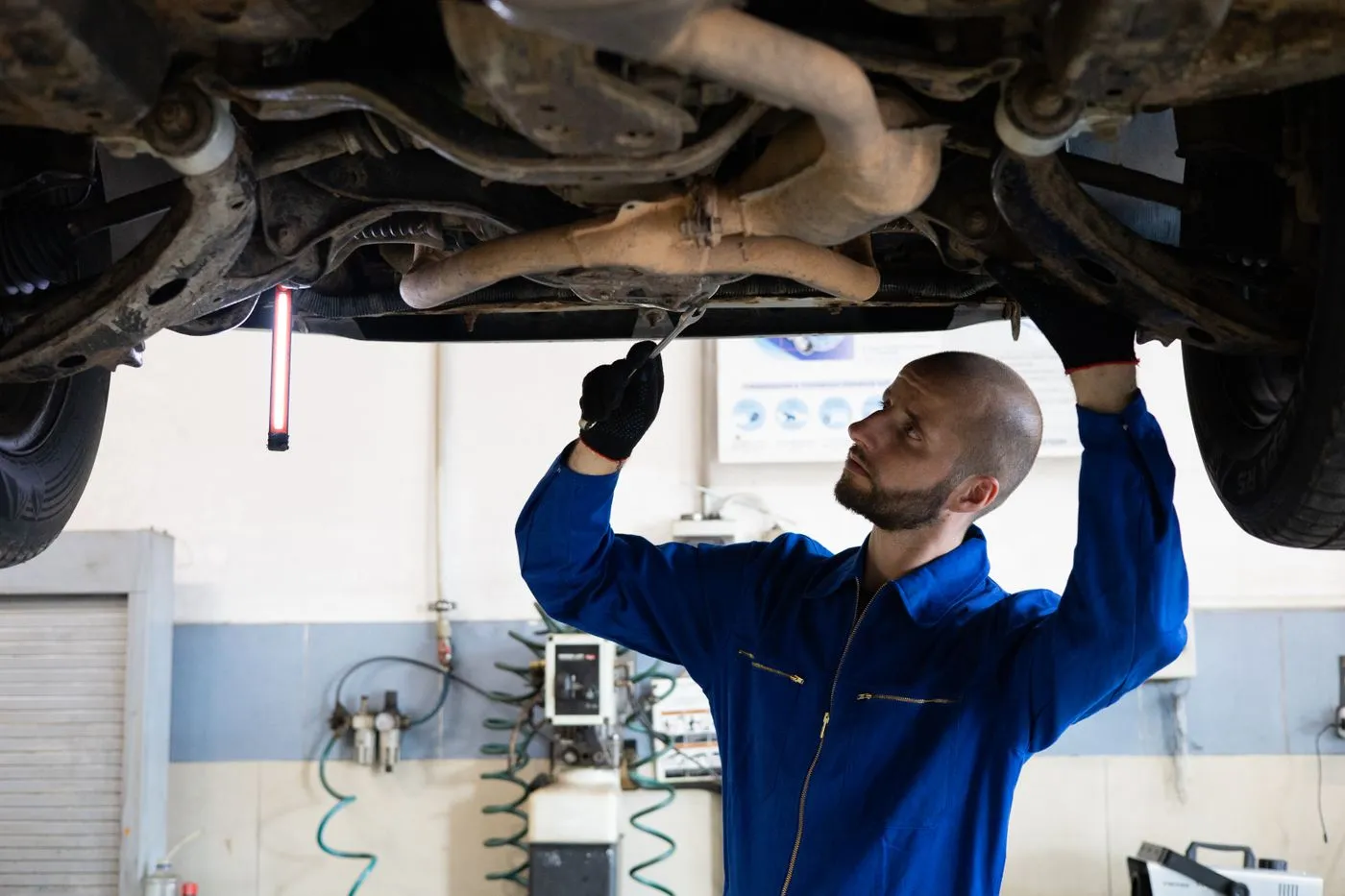 Mechanic working beneath a raised car in a garage. Photo by Artem Podrez on Pexels
