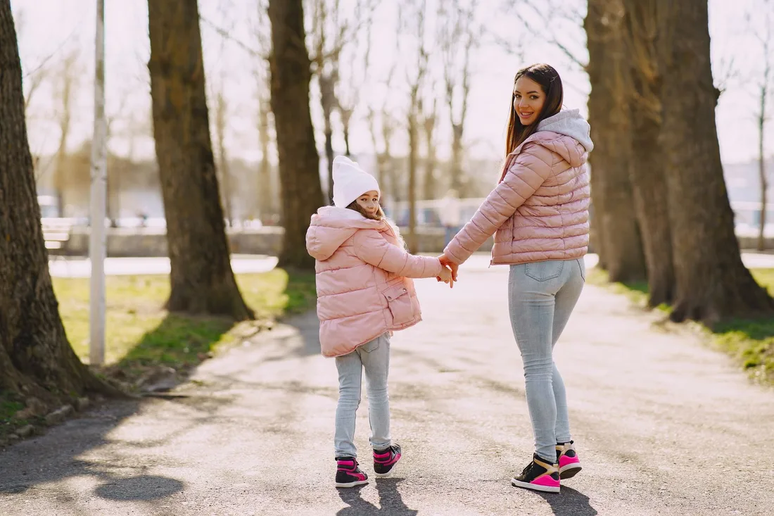 Mother and child holding hands walking along a sunny park path. Photo by Gustavo Fring on Pexels