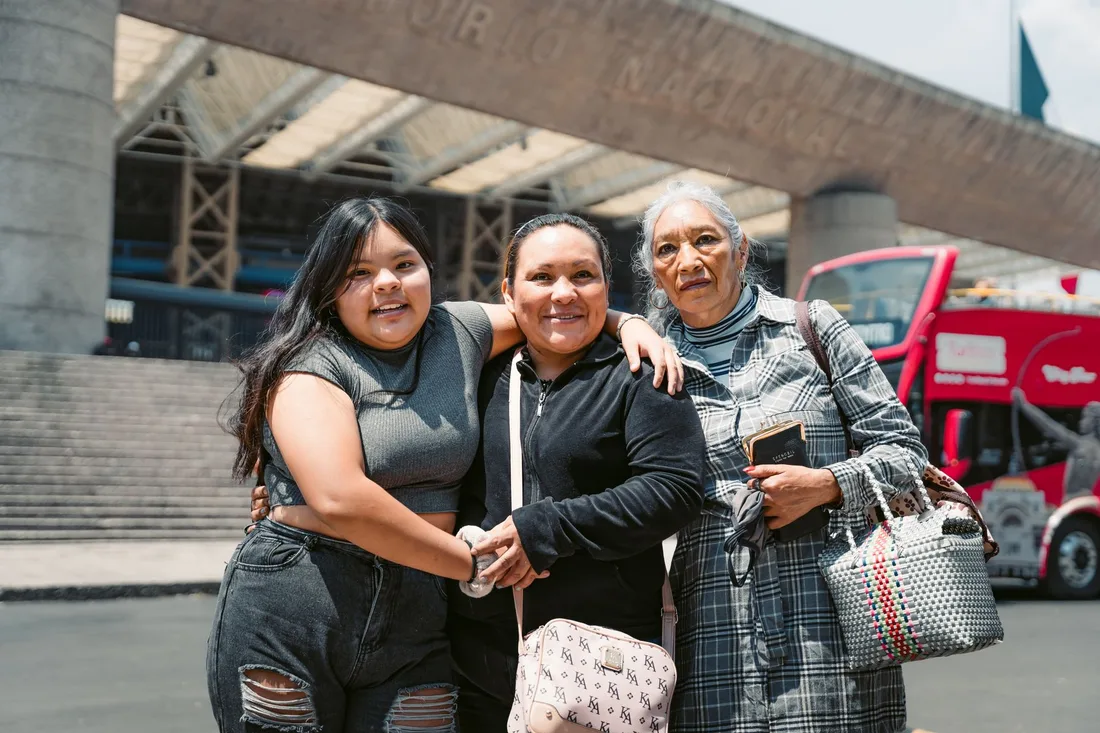 Group of smiling women embracing in a busy transit hall. Photo by Miguel González on Pexels