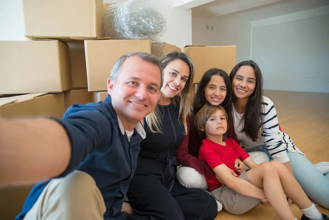 Smiling family taking a group selfie among boxes in their new home. Photo by Kampus Production on Pexels