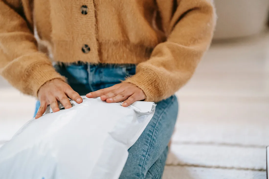 Woman in a cardigan holding a white padded mailer on her lap. Photo by Liza Summer on Pexels