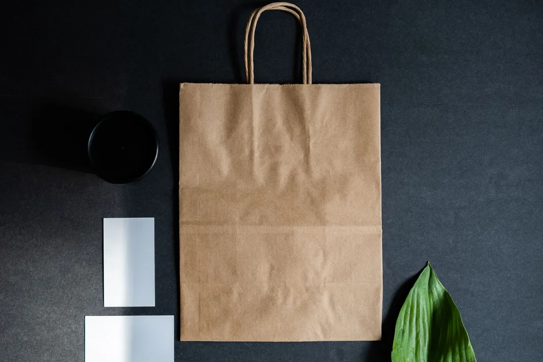 Stylish flat lay composition featuring a brown paper bag, green leaf, and black cup on a dark background.. Photo by PNW Production on Pexels