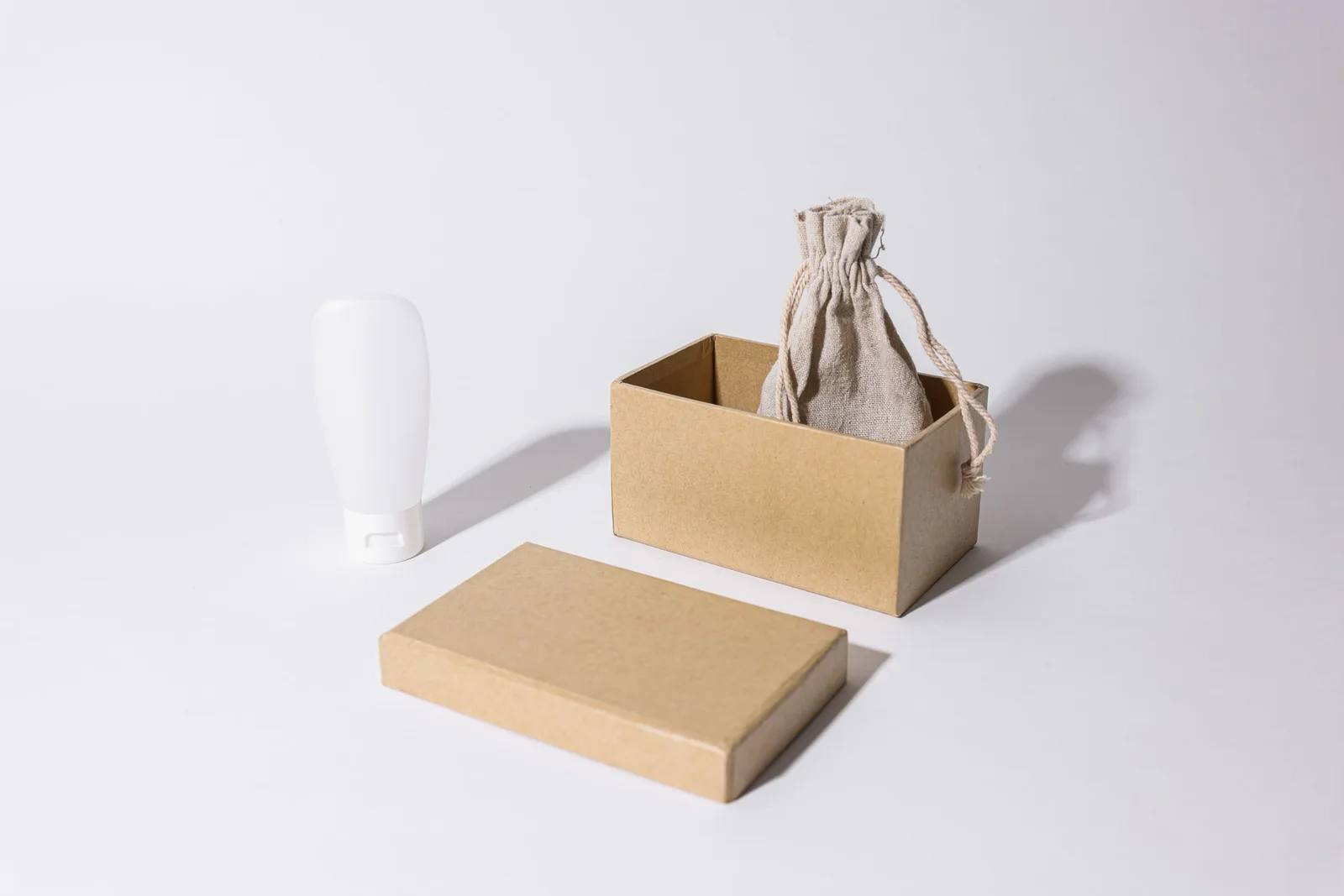 Stylish minimalist mockup featuring a cardboard box, linen pouch, and cream tube on a white background.. Photo by Cup of  Couple on Pexels