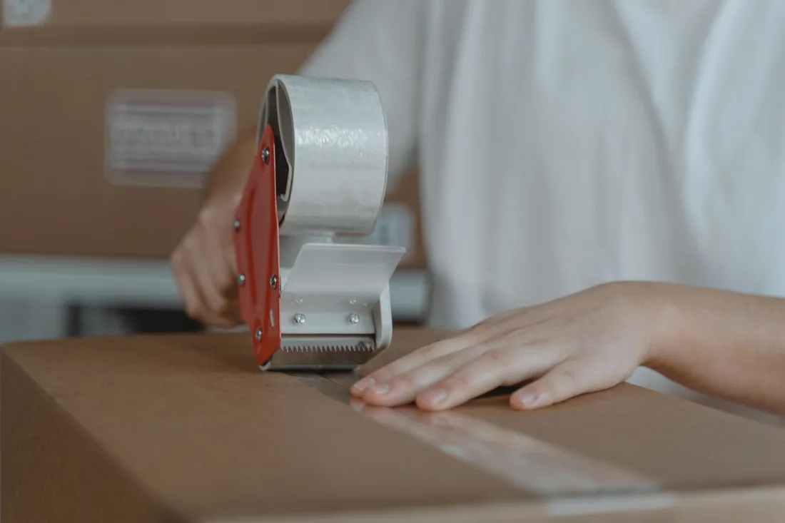 A person sealing a cardboard box with tape, emphasizing packaging and shipping processes.. Photo by Tima Miroshnichenko on Pexels
