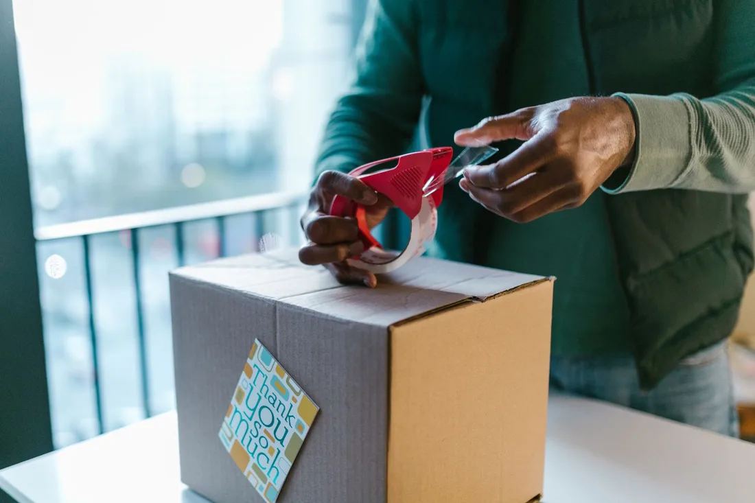 Close-up of man sealing a cardboard box with a tape dispenser indoors.. Photo by RDNE Stock project on Pexels