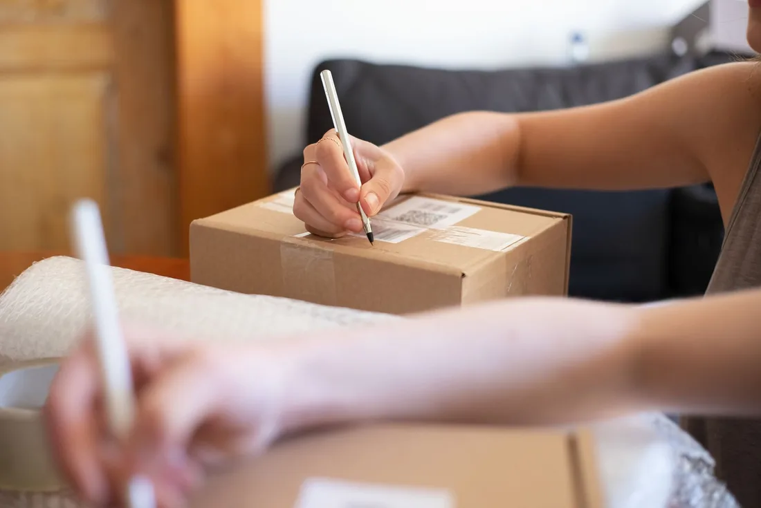 Close-up of hands labeling a cardboard box for online shipping from a home office.. Photo by Kampus Production on Pexels