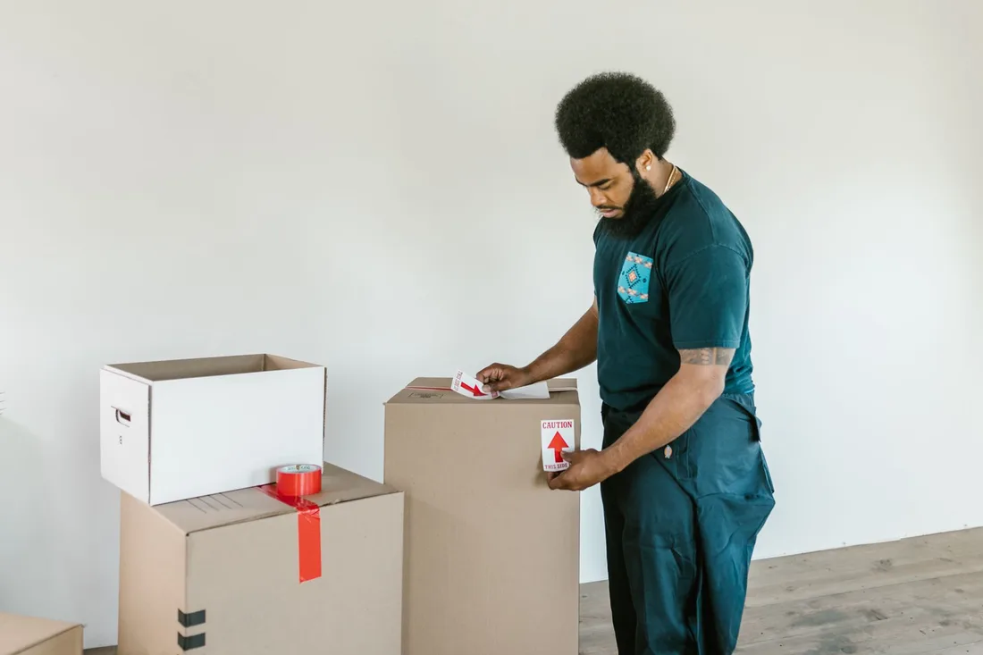 A man preparing cardboard moving boxes with caution stickers in a bright indoor setting.. Photo by RDNE Stock project on Pexels