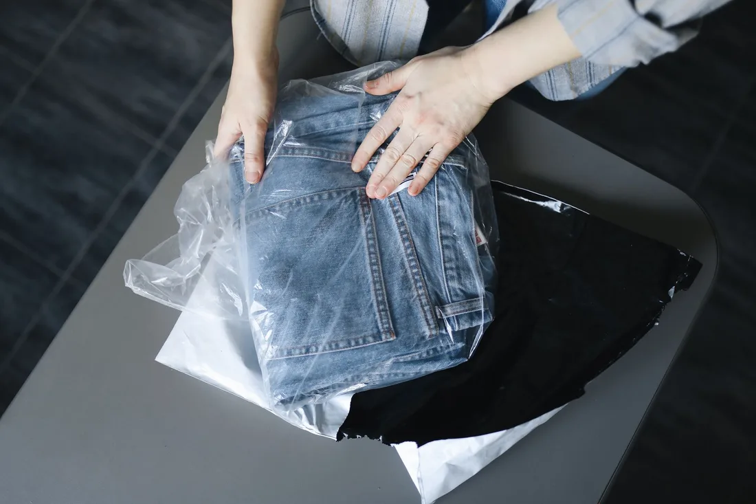 Woman carefully packs blue jeans into a plastic bag on a dark surface.. Photo by Polina Tankilevitch on Pexels