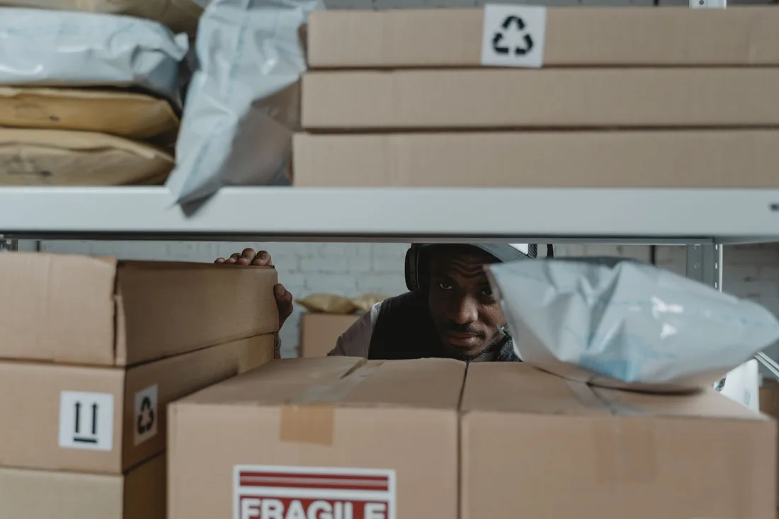 Warehouse worker inspecting shipment packages on shelves, ensuring quality and accuracy in logistics.. Photo by Tima Miroshnichenko on Pexels