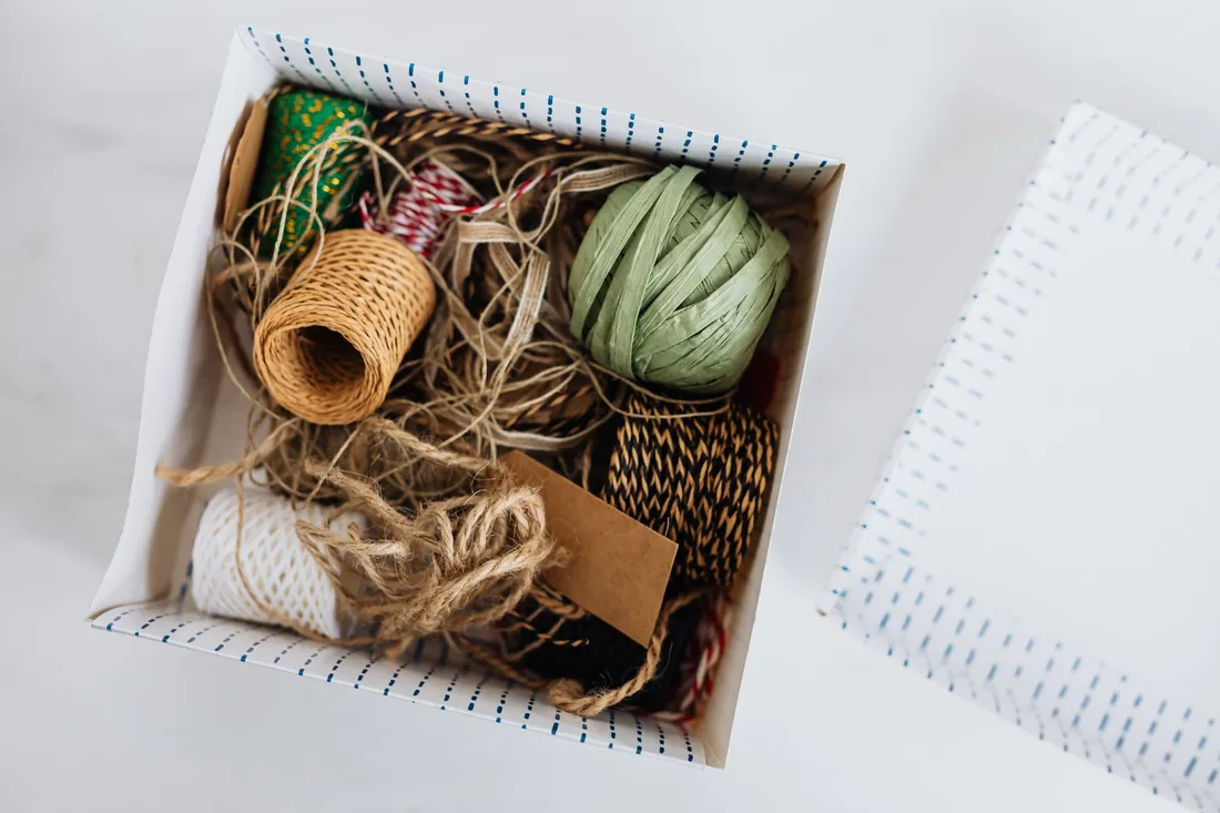 Top view of carton box filled with assorted ribbons and ropes for holiday presents and gifts wrapping and blank brown cardboard card placed on white table near cover. Photo by https://kaboompics.com/ on Pexels