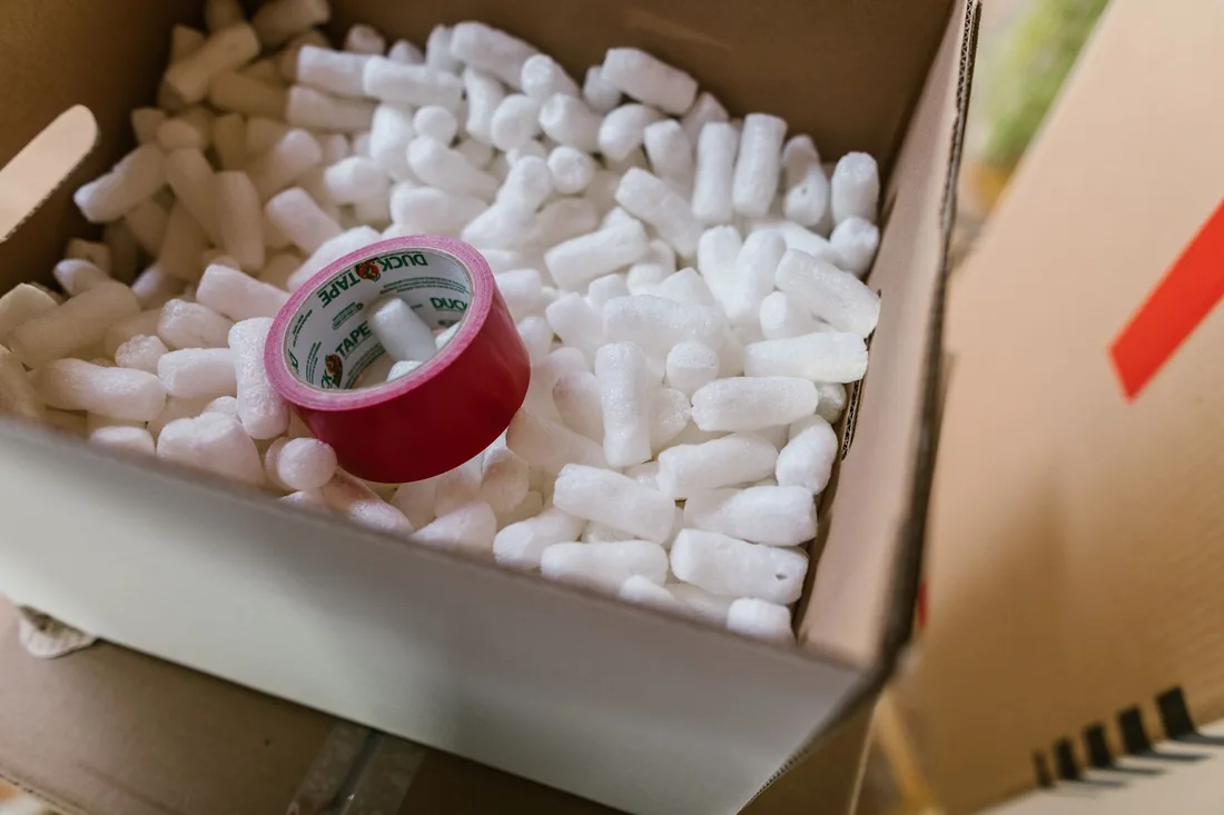 Cardboard box filled with packing peanuts and a roll of red tape. Photo by RDNE Stock project on Pexels