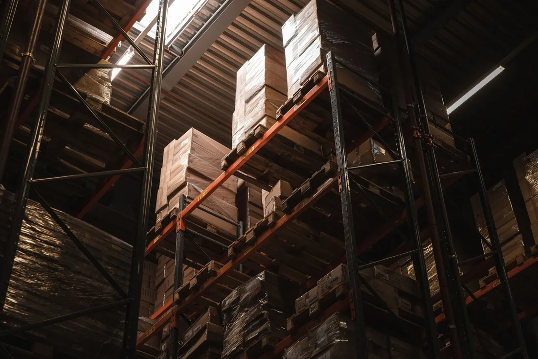 Interior view of a warehouse with stacked cardboard boxes on high shelves, showcasing storage and logistics.. Photo by Ryan Klaus on Pexels