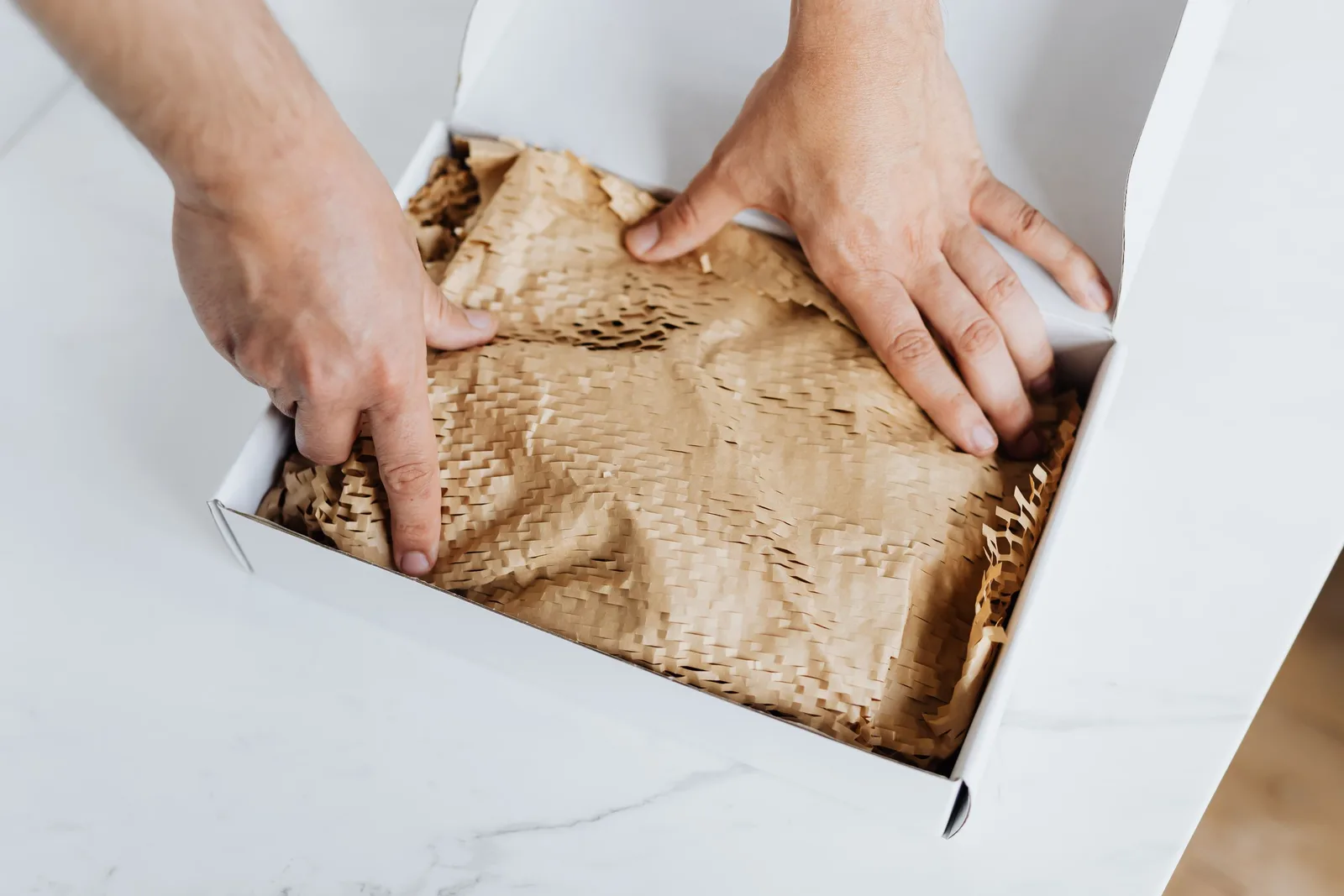 Hands laying kraft paper padding into a white box for eco friendly packing. Photo by https://kaboompics.com/ on Pexels