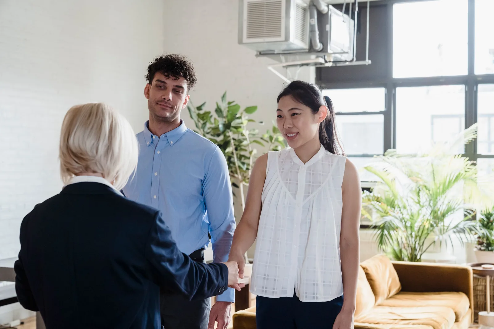 Leasing agent shaking hands with a young couple inside a bright apartment with plants. Photo by Timur Weber on Pexels
