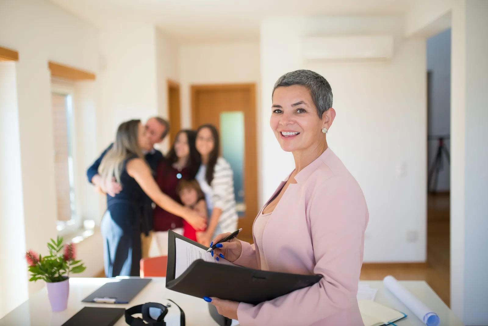 Smiling letting agent in pink blazer holding a folder in a bright flat. Photo by Kampus Production on Pexels