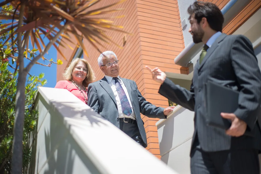 Older couple on a sunny balcony with a real estate agent in a suit. Photo by Kampus Production on Pexels