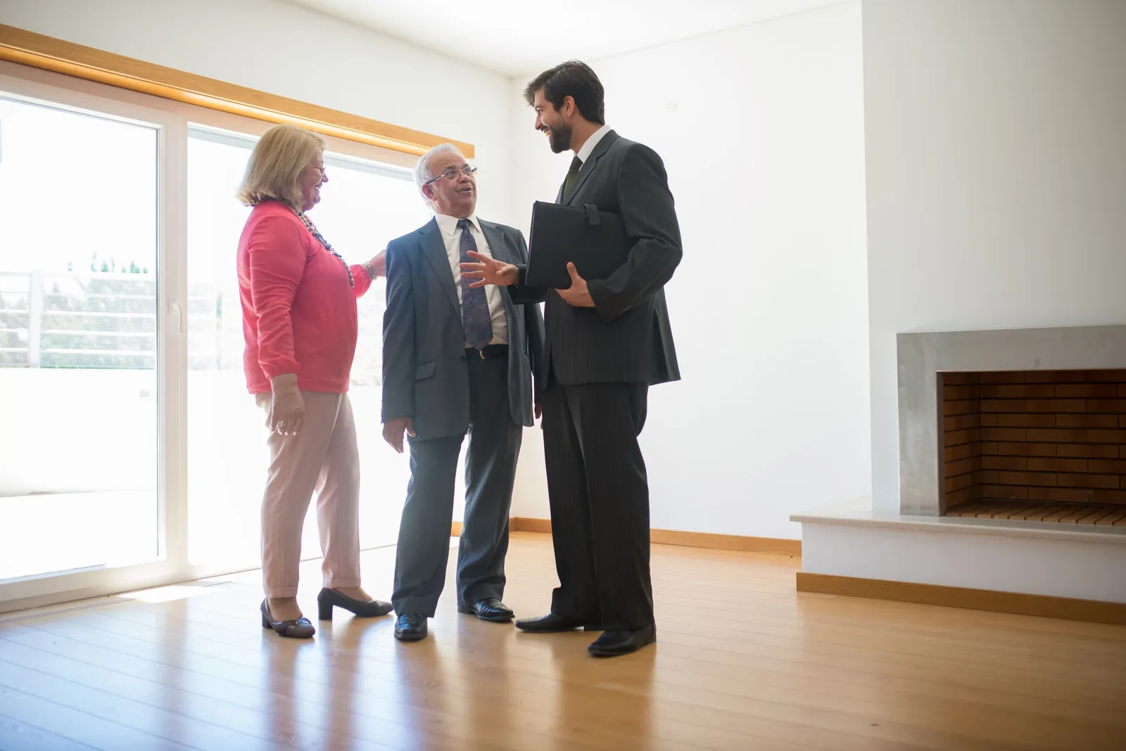 Agent in suit showing a bright, spacious home with a fireplace to two clients. Photo by Kampus Production on Pexels