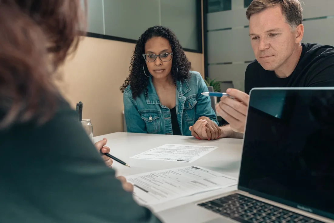 Couple reviewing mortgage paperwork with an adviser at a table with a laptop. Photo by Kindel Media on Pexels
