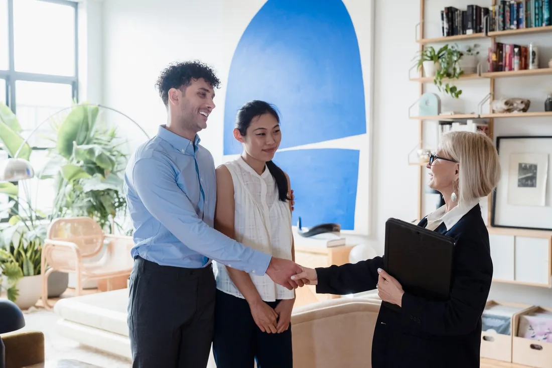 Couple shaking hands with a sales agent inside a bright, plant-filled show home. Photo by Timur Weber on Pexels