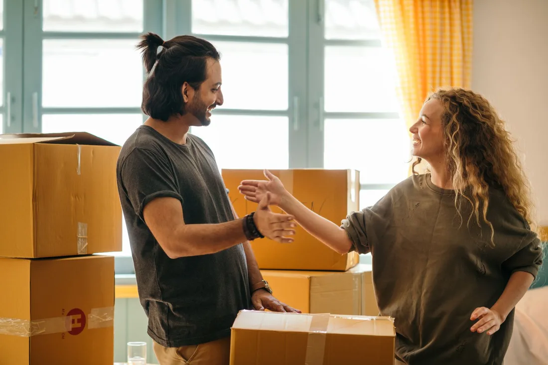 Happy couple chatting among moving boxes in a sunlit new apartment. Photo by Ketut Subiyanto on Pexels