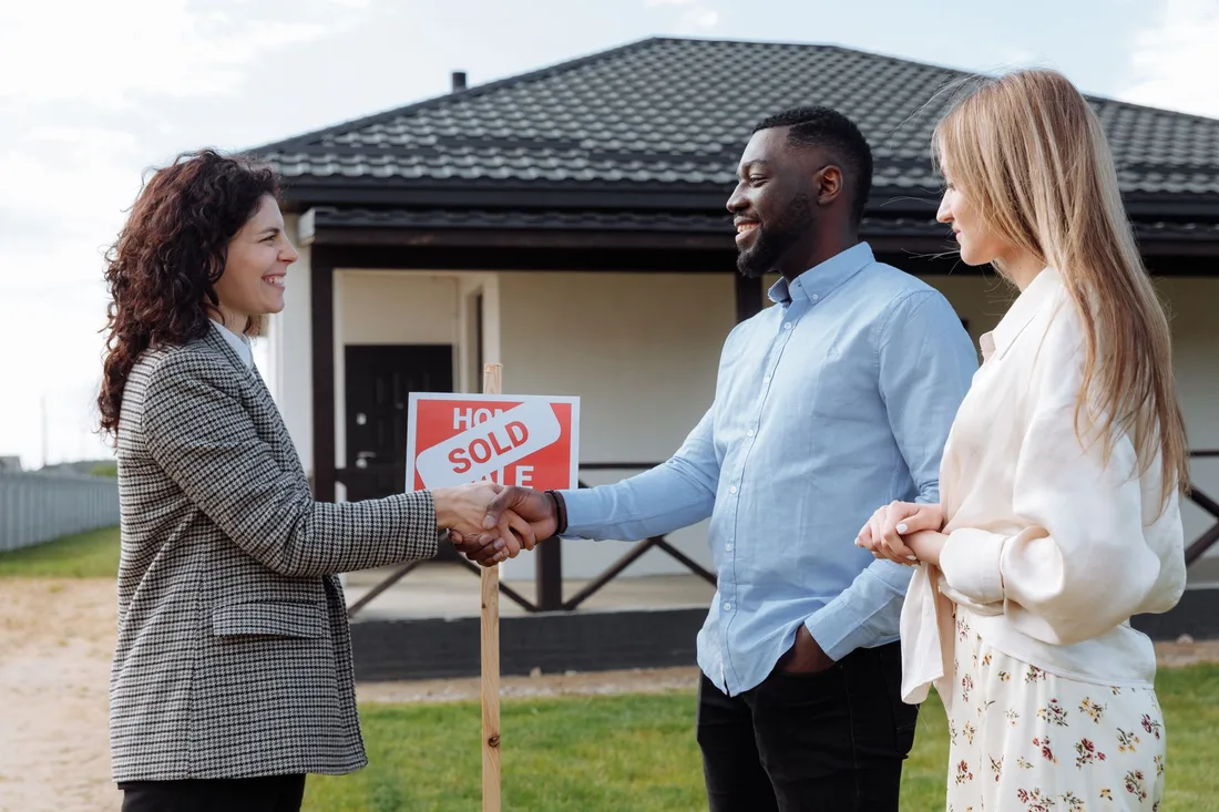 Agent shaking hands with happy buyers in front of a house with a sold sign. Photo by Thirdman on Pexels
