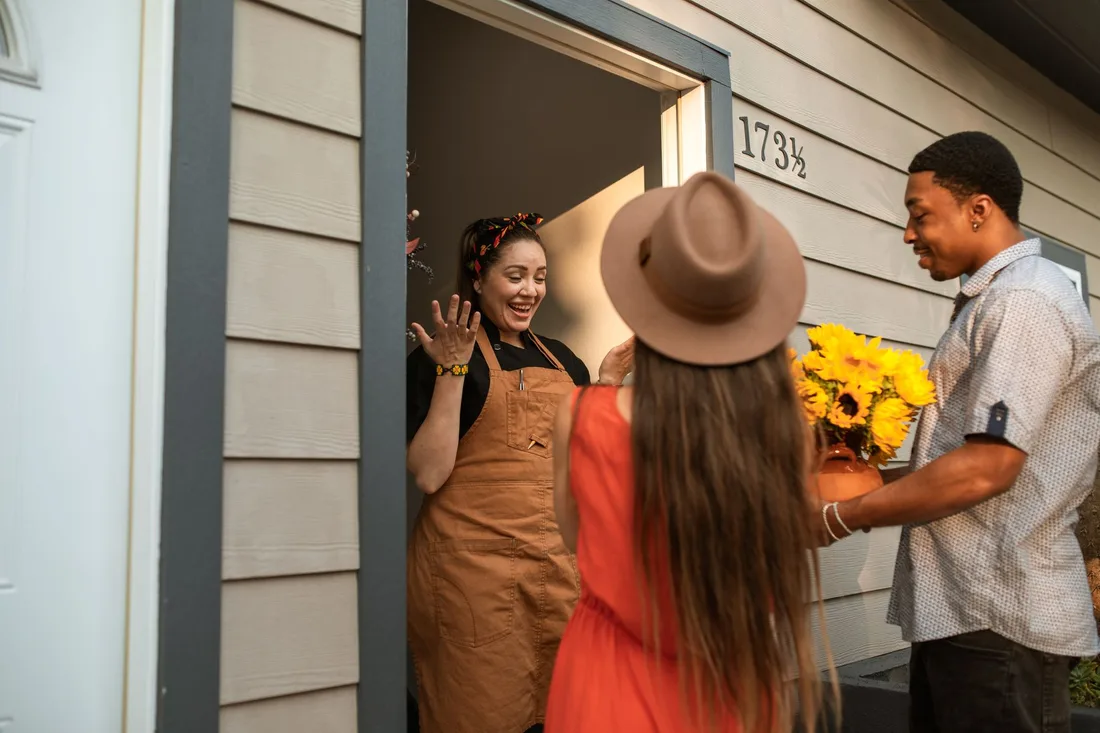 Host in doorway greeting smiling guest holding yellow flowers at a holiday rental house. Photo by RDNE Stock project on Pexels