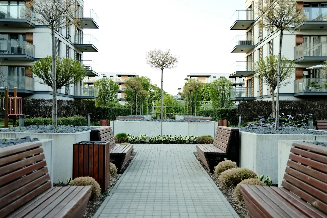 Tidy apartment complex courtyard with paved path, benches and landscaped planters. Photo by Egor Komarov on Pexels
